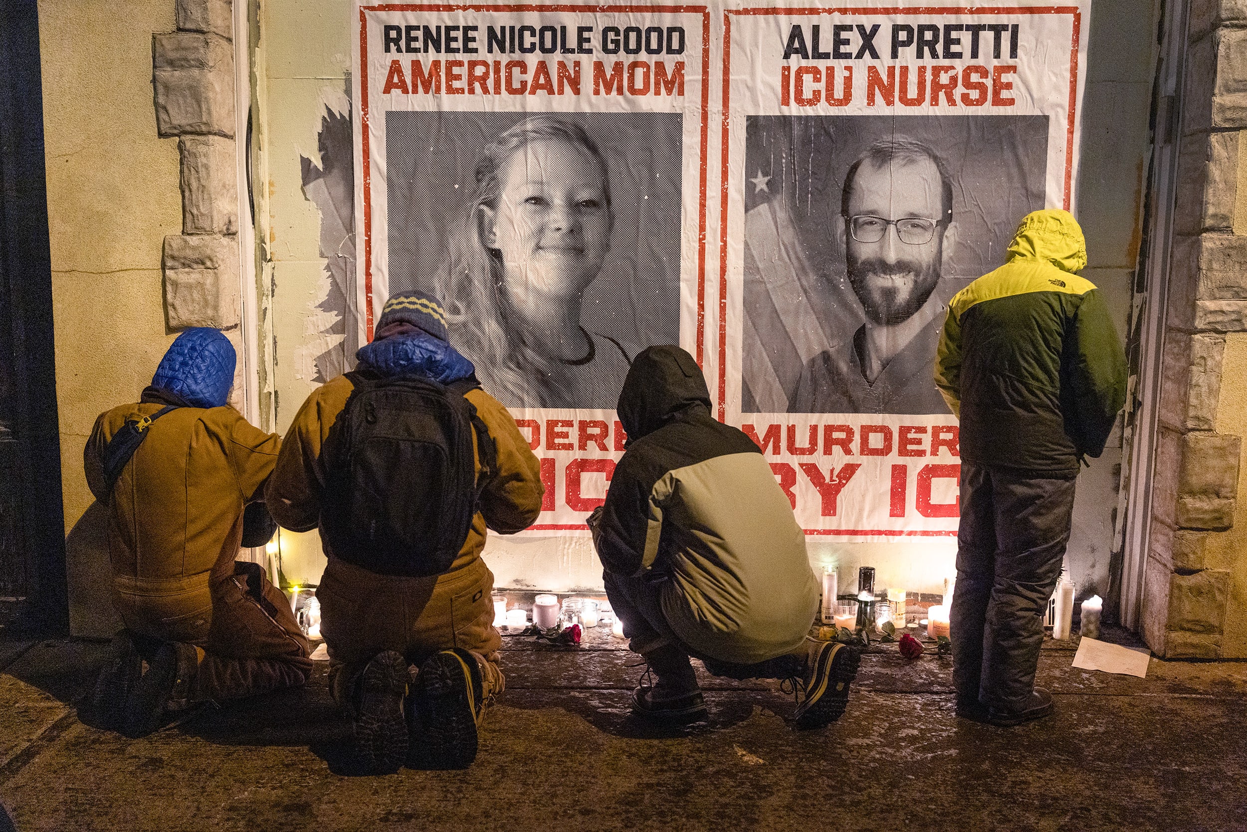 Four people stand in front of a candle-lit vigil at night.