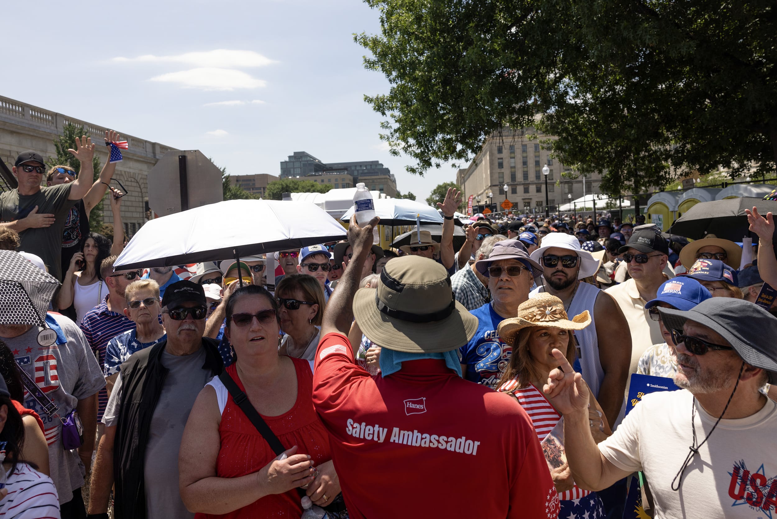 People with umbrellas and sun hats all raise their hands for a bottle of water from a safety ambassador.