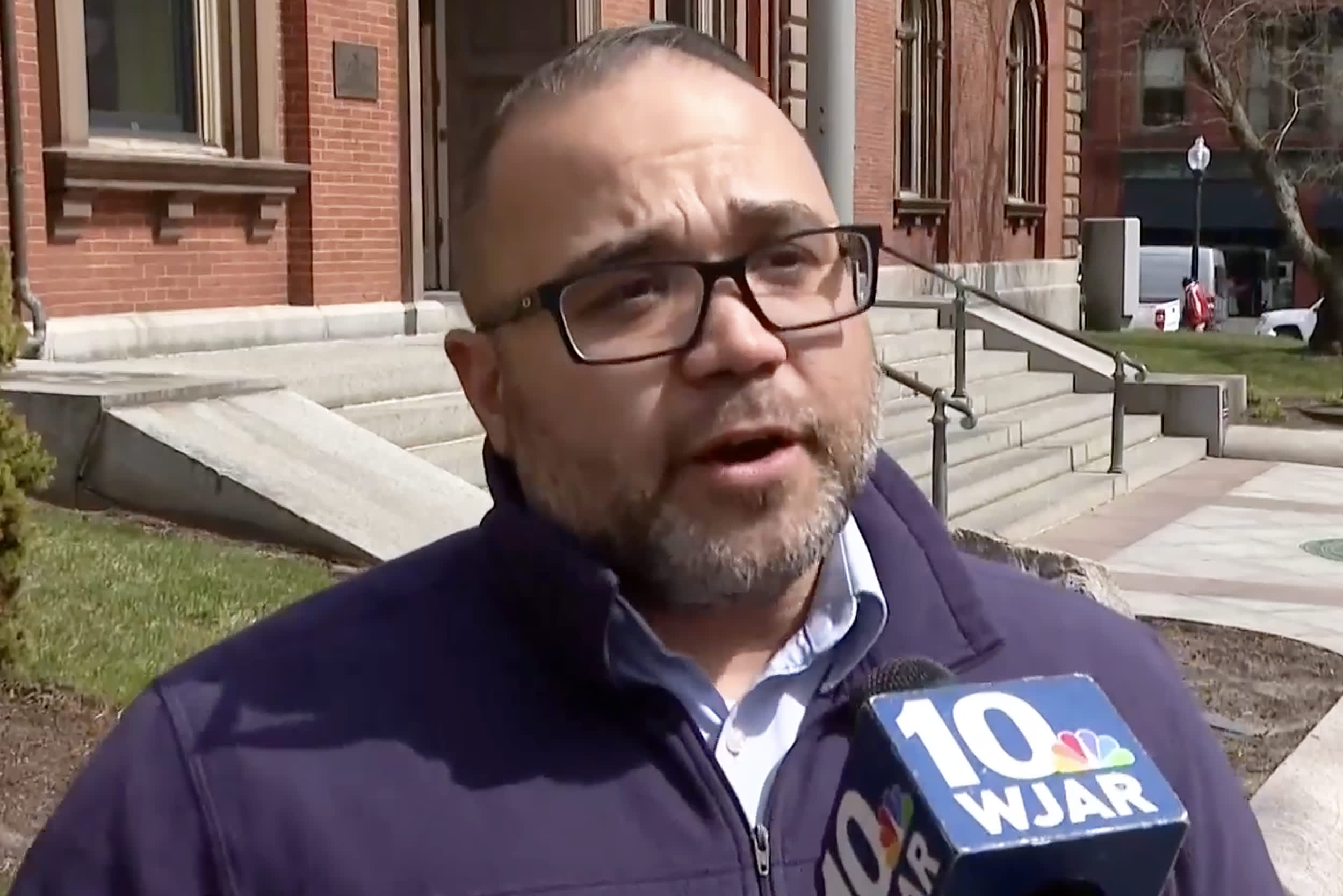 Image: Shawn Oliver speaking into a WJAR branded microphone outside.