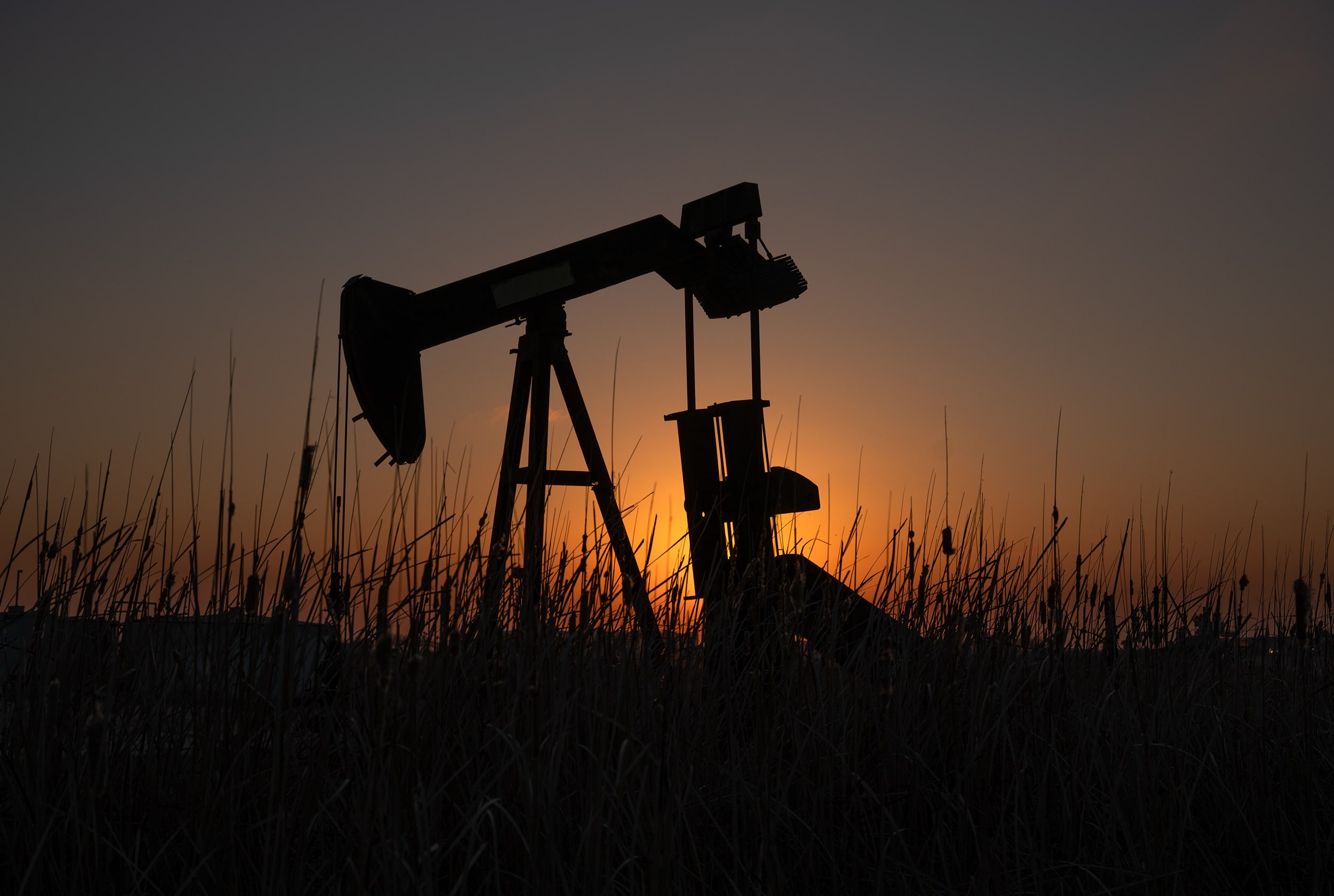 The sun sets behind an oil pump jack creating a silhouette.