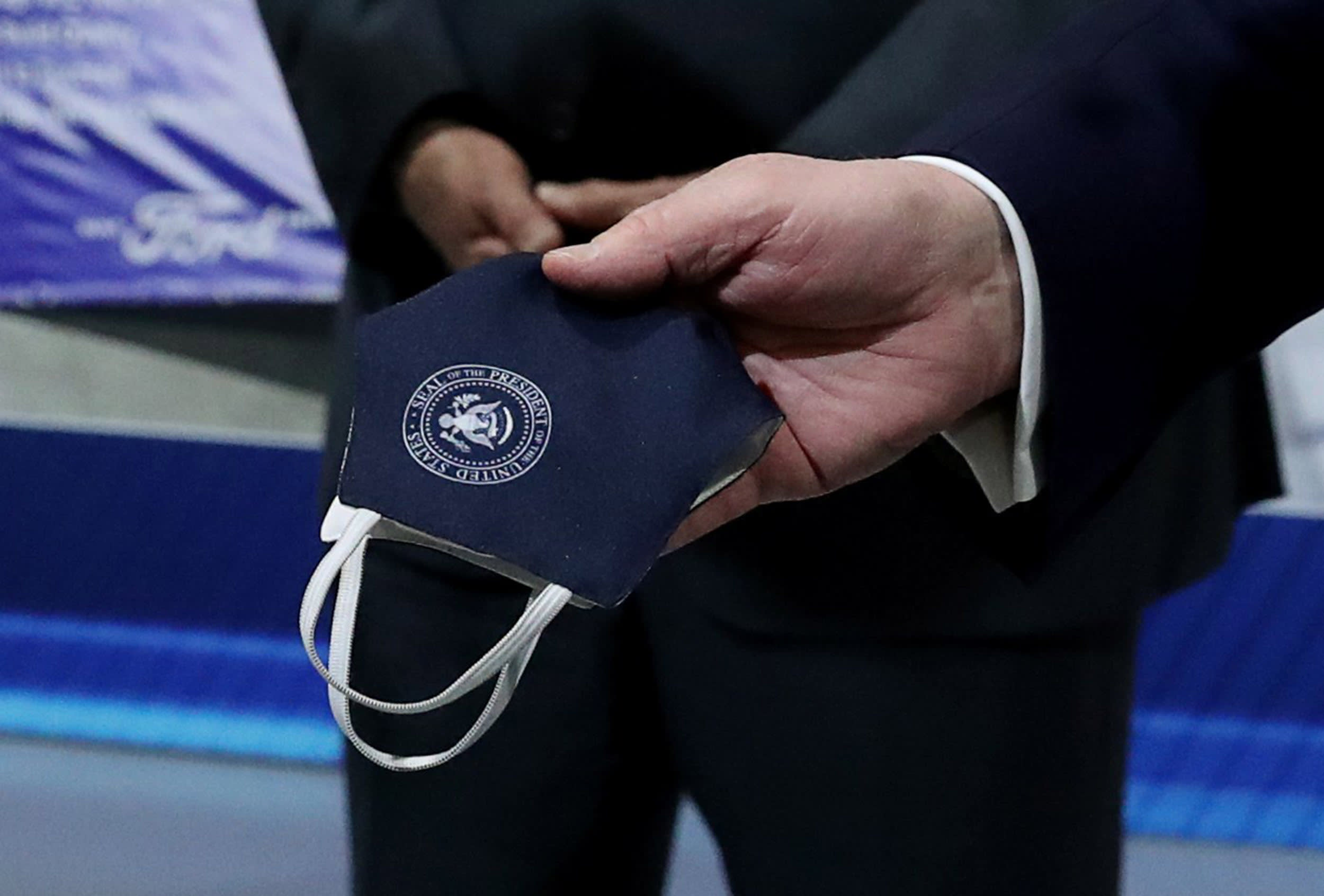Image: President Donald Trump holds a protective face mask with a presidential seal on it that he said he had been wearing earlier in his tour at the Ford Rawsonville Components Plant