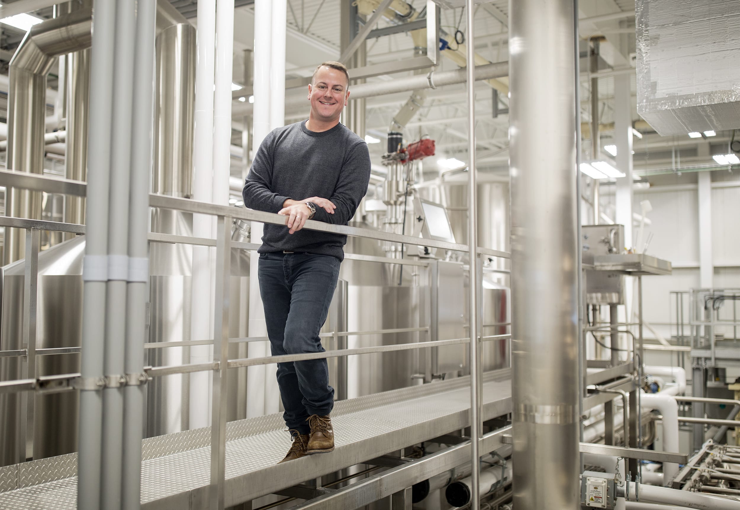 A man standing on an elevated walkway inside a brewery.