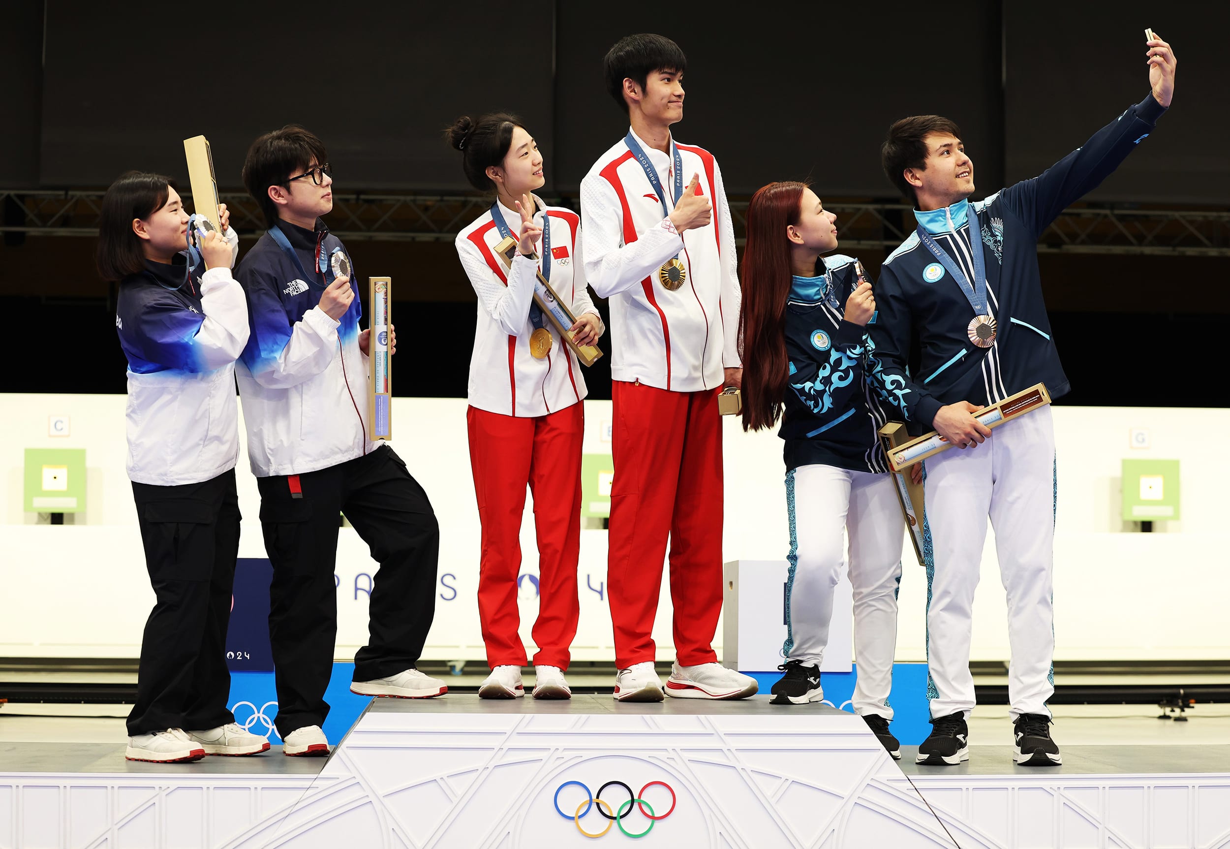 CHATEAUROUX, FRANCE - JULY 27: Gold medalists Yuting Huang and Lihao Sheng of Team People’s Republic of China (L), Silver medalists Hajun Park and Jihyeon Keum of Team Republic of Korea (L) and Bronze medalists Alexandra Le and Islam Satpayev of Team Kazakhstan (R) take a selfie on the podium during the Shooting medal ceremony after the 10m Air Rifle Mixed Team on day one of the Olympic Games Paris 2024 at Chateauroux Shooting Centre on July 27, 2024 in Chateauroux, France.
