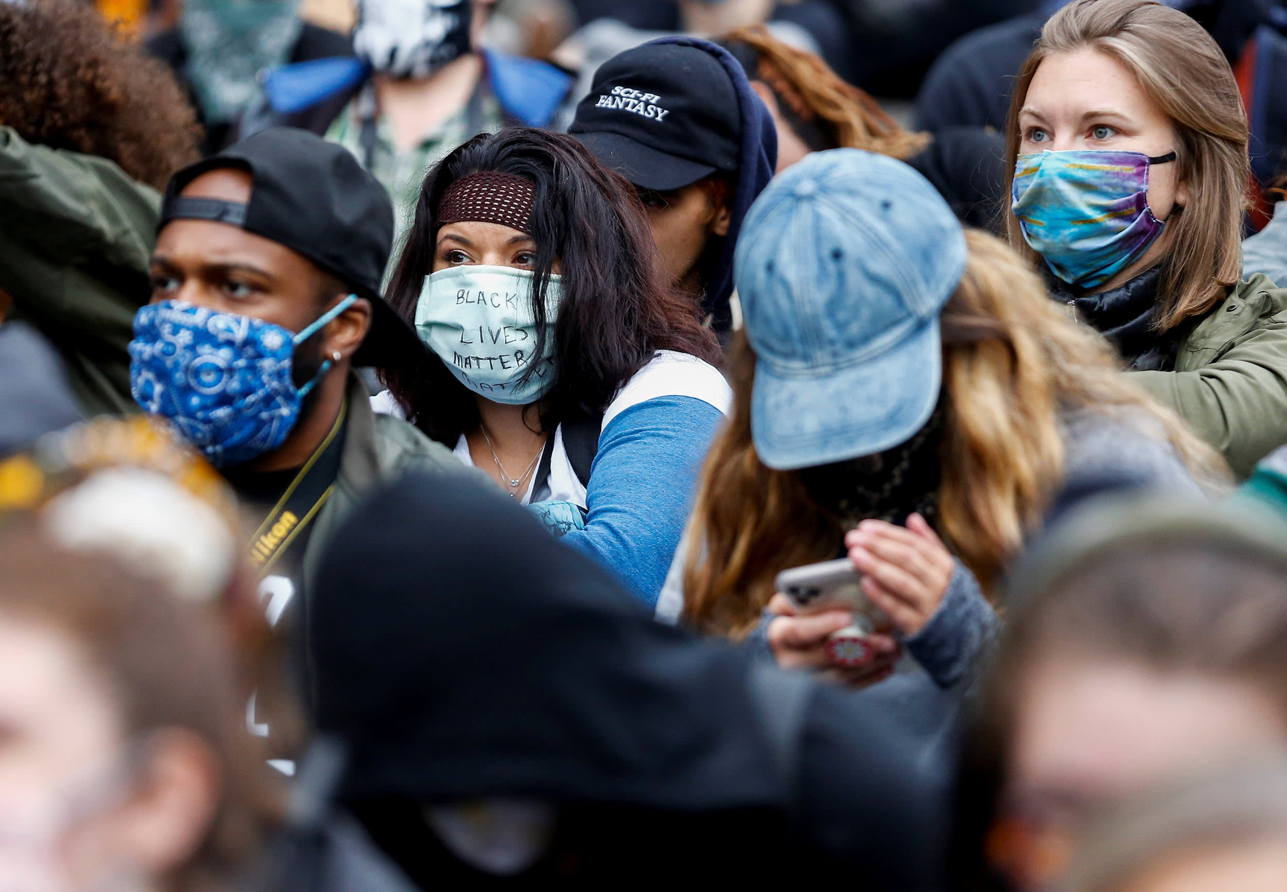Image: A protester wears a surgical mask with "Black Lives Matter" written on the front while protesters gather outside the Seattle Office of Emergency Management to protest against police brutality and the death in police custody of George Floyd