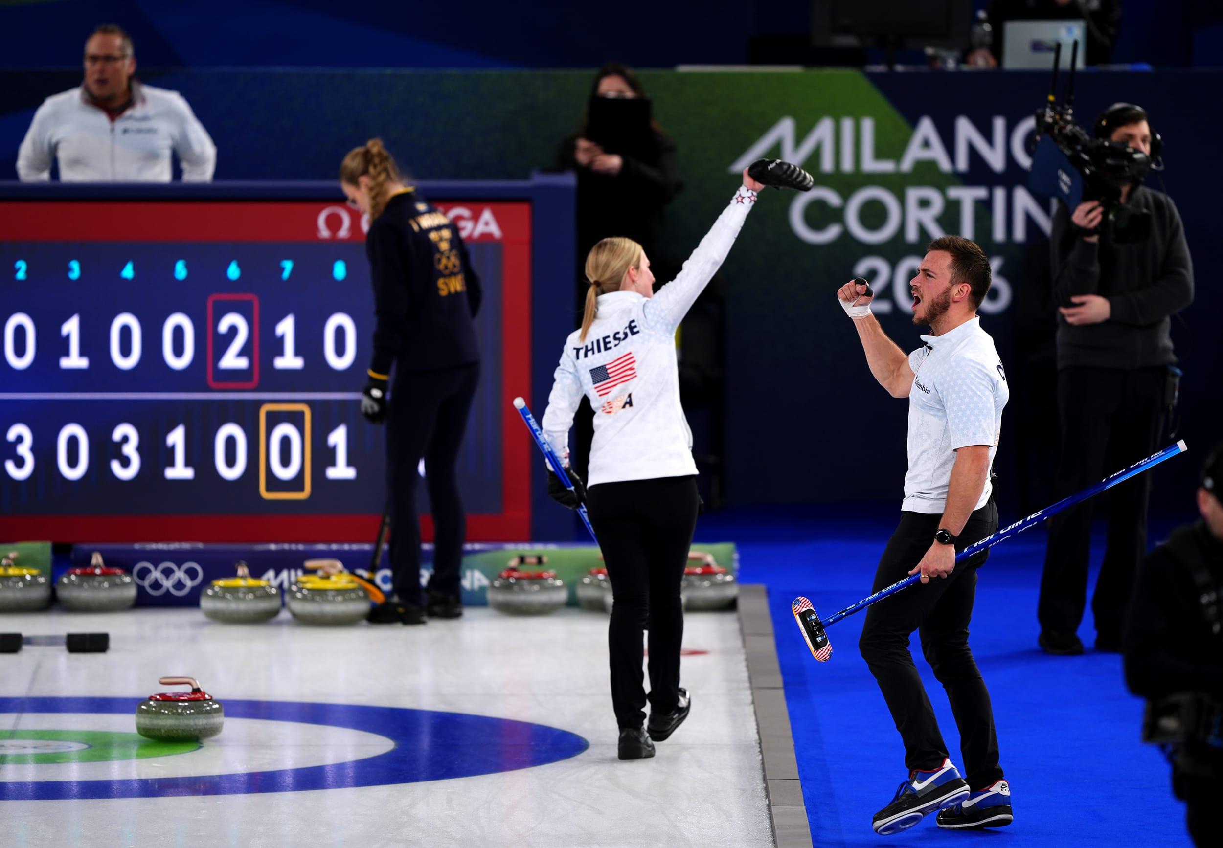 Cory Thiesse and Korey Dropkin both raise their hands in the air in triumph while celebrating an Olympic win.