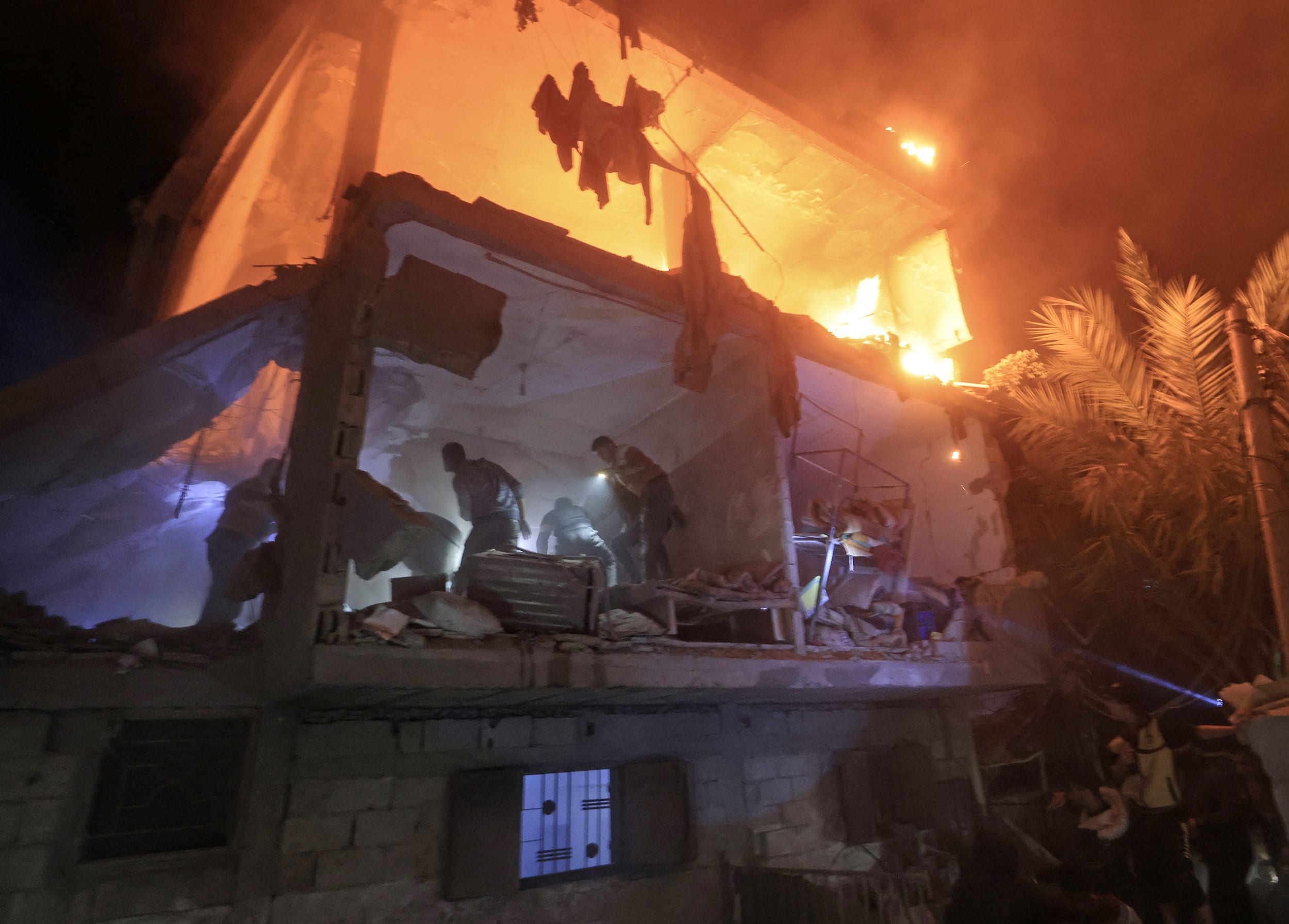 People use the lights on their telephones to search for victims amid the rubble of a smoldering building in Rafah in the southern Gaza Strip on Dec. 6, 2023.