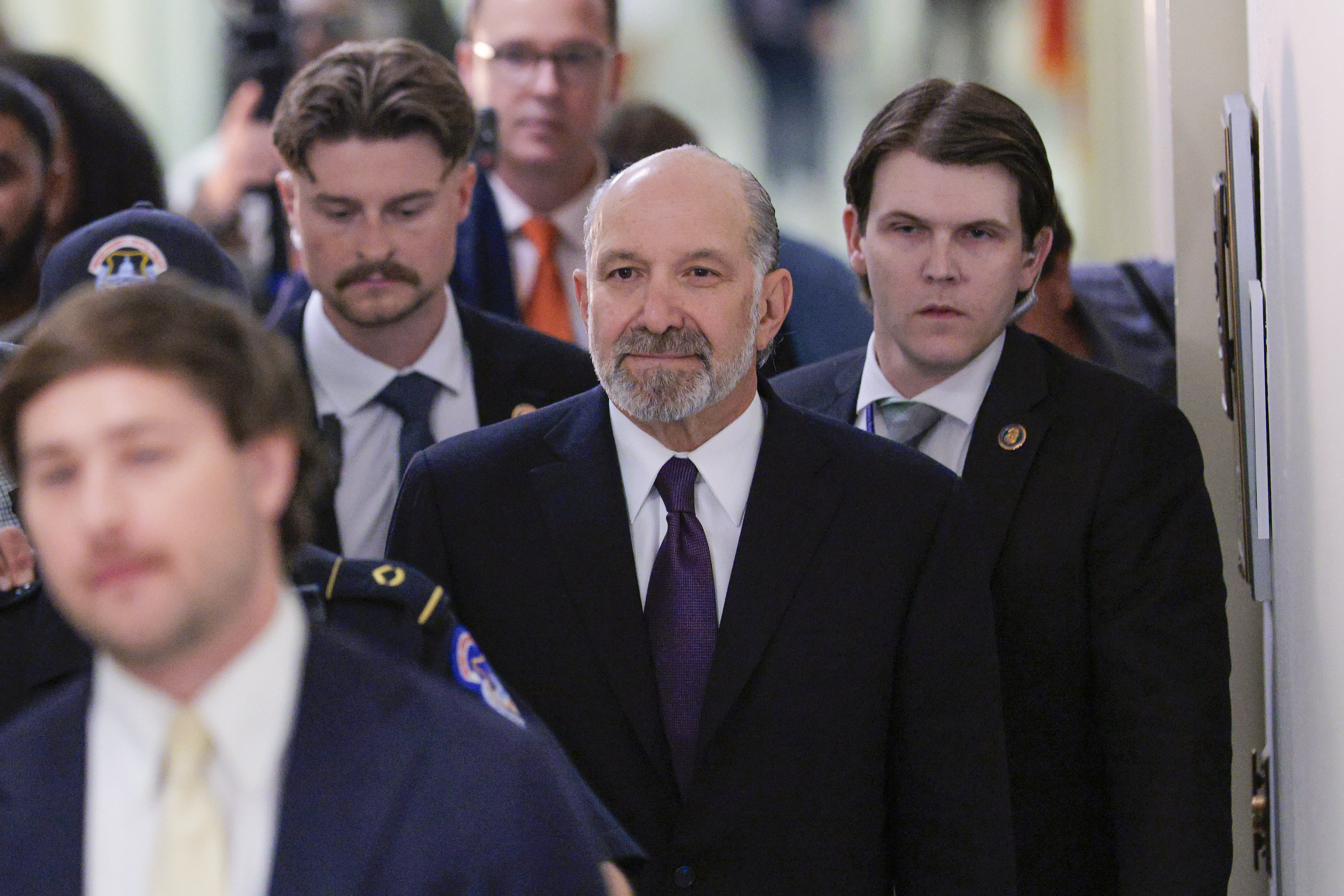 Howard Lutnick walking down a hallway at the U.S. Capitol surrounded by aides.