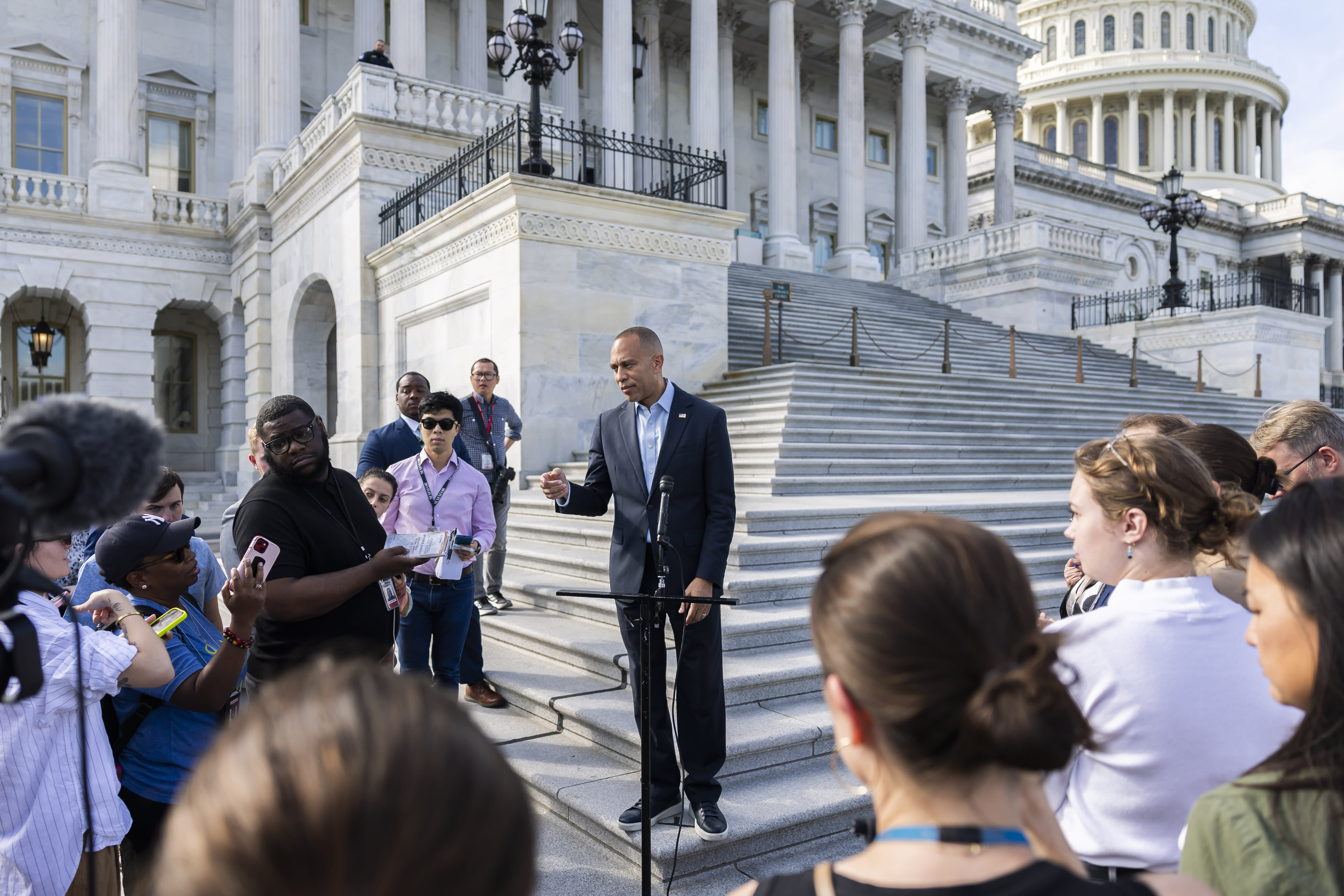 Hakeem Jeffries stands in front of a microphone on the steps of the U.S. Capitol, surrounded by reporters. 