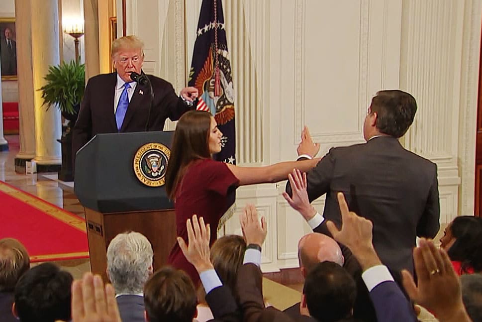 A White House staff member reaches for the microphone held by CNN's Jim Acosta