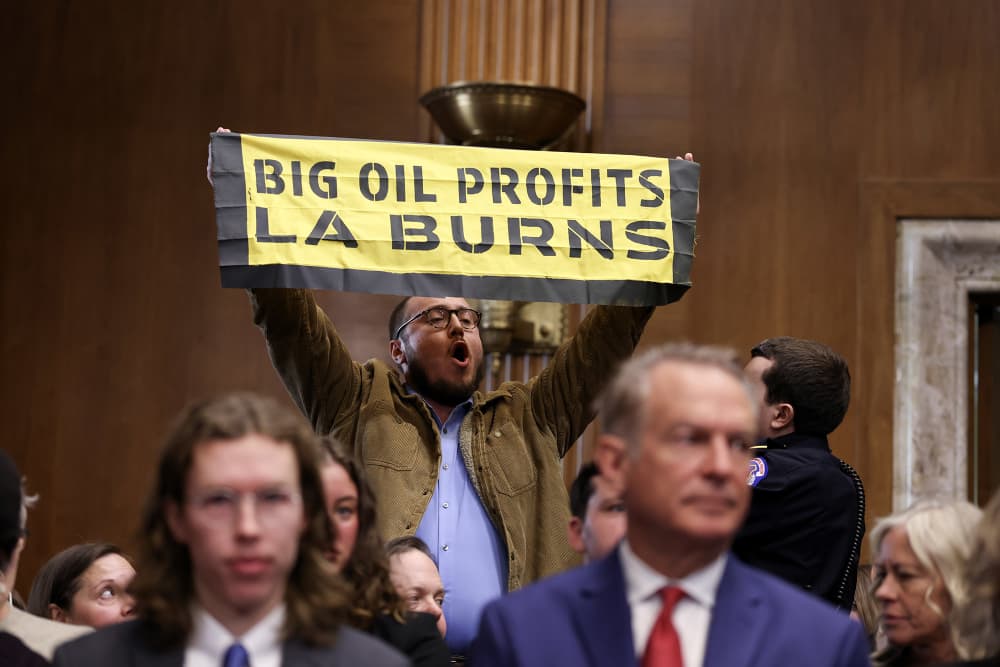 A protester holds up a sign as Chris Wright testifies on Jan. 15, 2025.