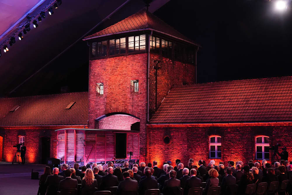 Guests sit in front of the main gate of the Auschwitz-Birkenau camp