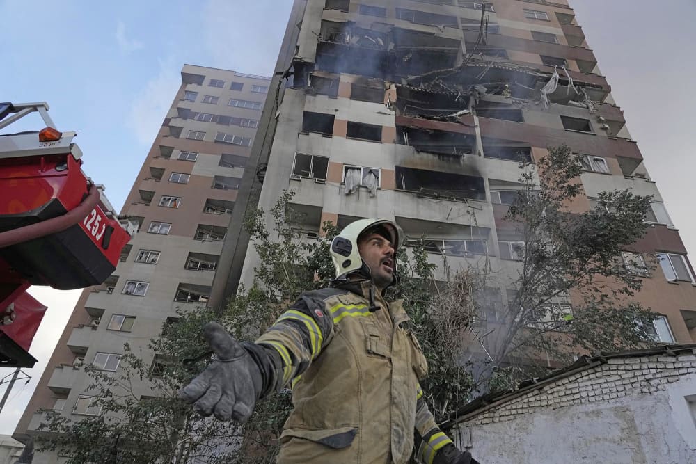 A firefighter calls out his colleagues at the scene of an explosion in a residence compound in northern Tehran, Iran, Friday, June 13, 2025.