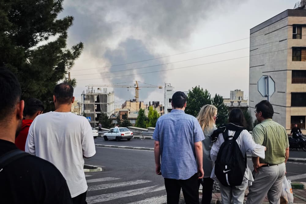 Smoke rises in the distance as people look on