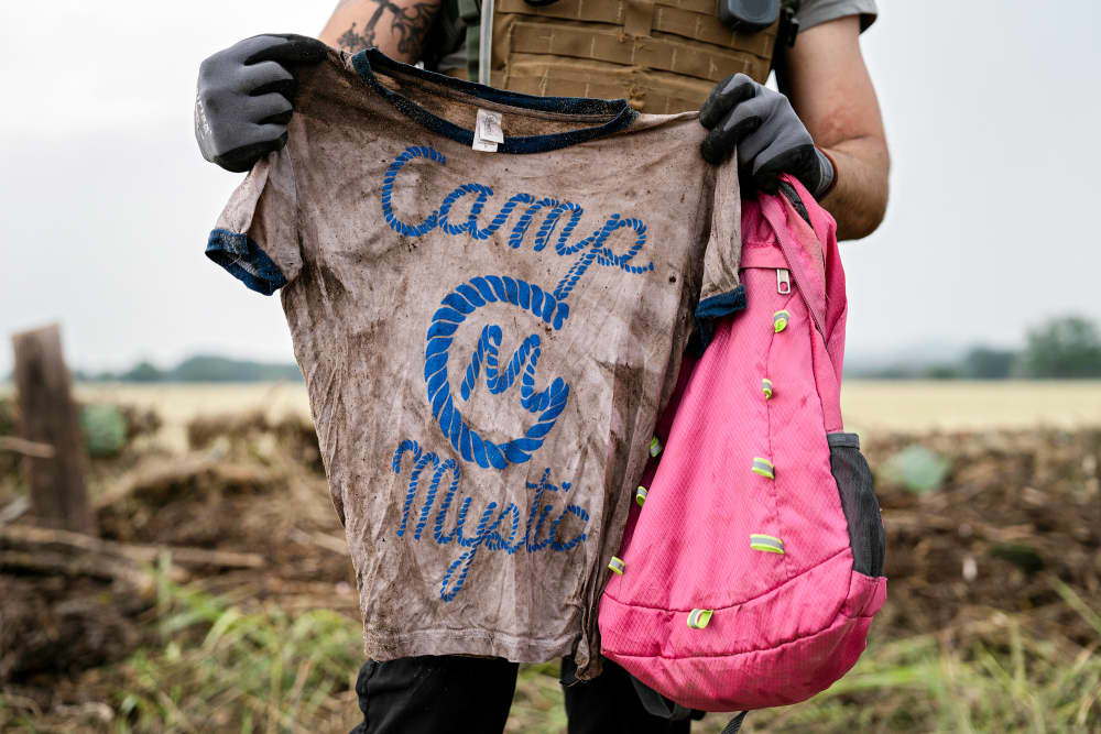 A search and rescue volunteer holds a T-shirt and backpack with the words Camp Mystic on them