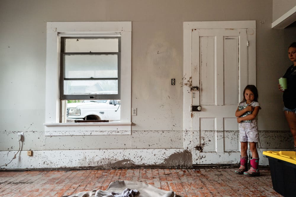A little girl stands by the doorway of a room with flood damage