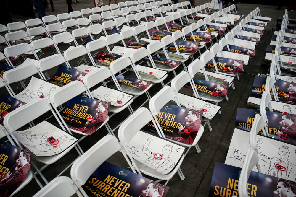 White chairs with Charlie Kirk photos laid on the seats with text that reqads "Never Surrender"