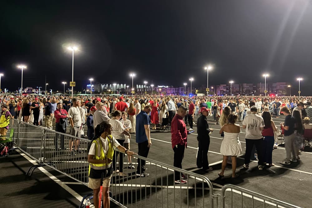A crowd of people wait outside in a parking lot