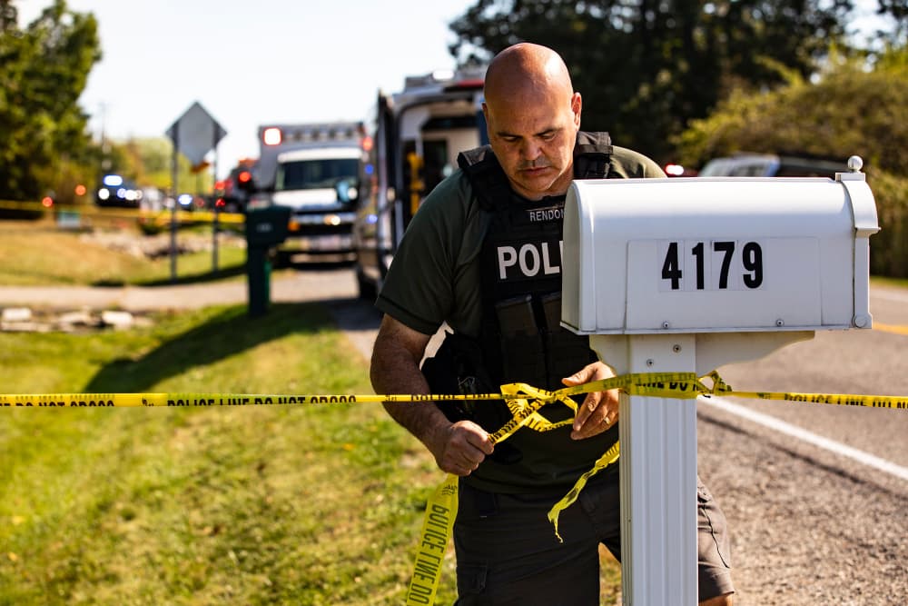 A police officer tapes off an area, tying the police tape around a mailbox