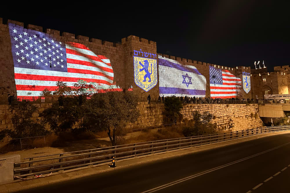 U.S. and Israel flags projected onto the side of a building along a freeway at night