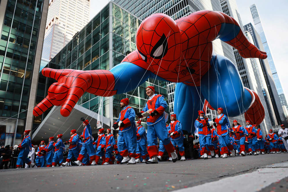 A spiderman balloon carried by hundred of people dressed like spiderman on the street outside