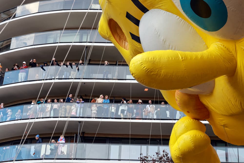 People on balconies watch a giant Spongebob balloon pass by
