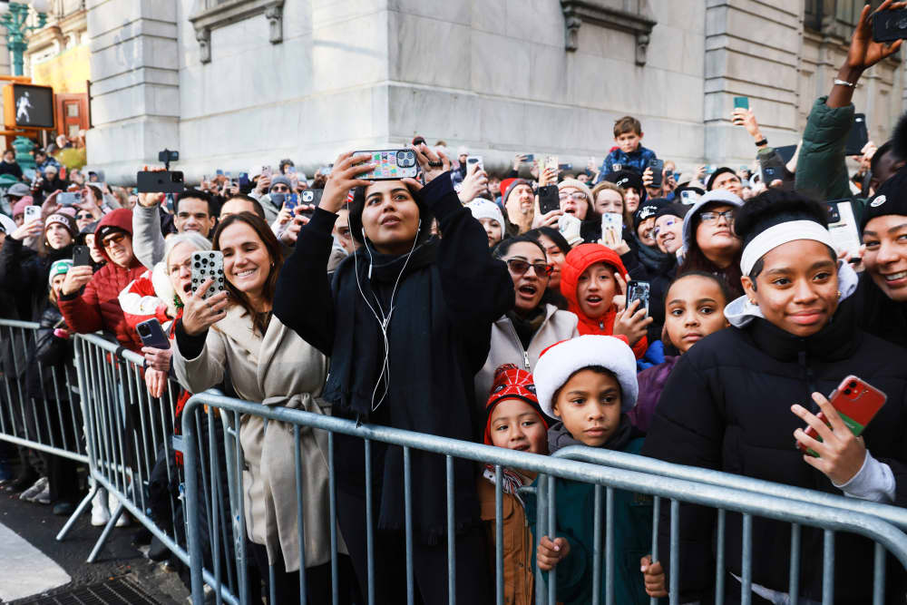 People watch the parade from behind a guard rail on the street
