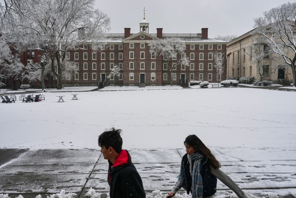 Two people walk past a building while it's snowy outside