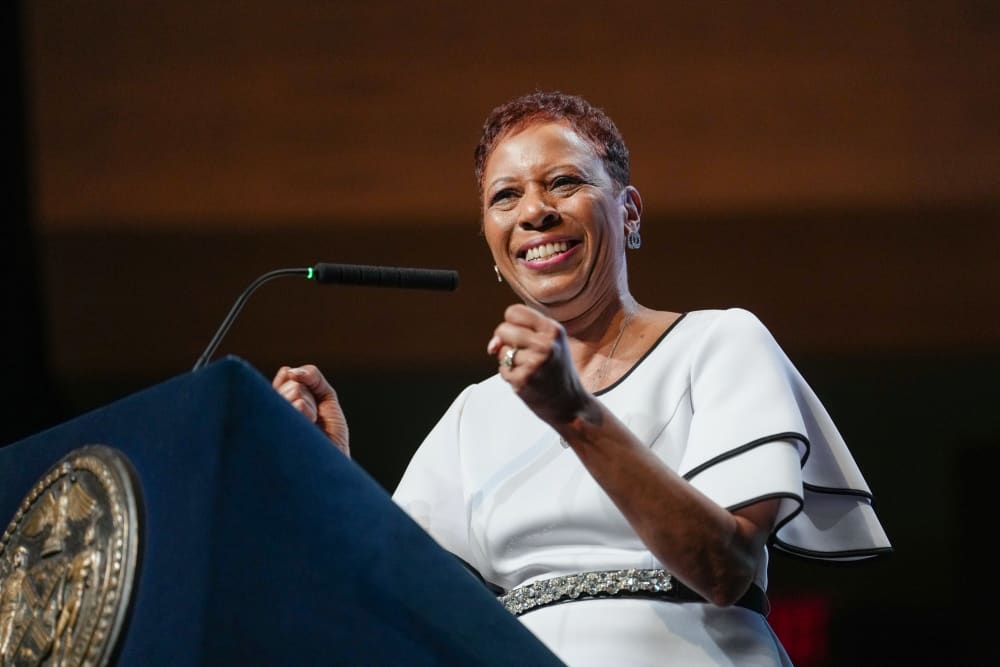 Adrienne Adams stands at a podium and smiles