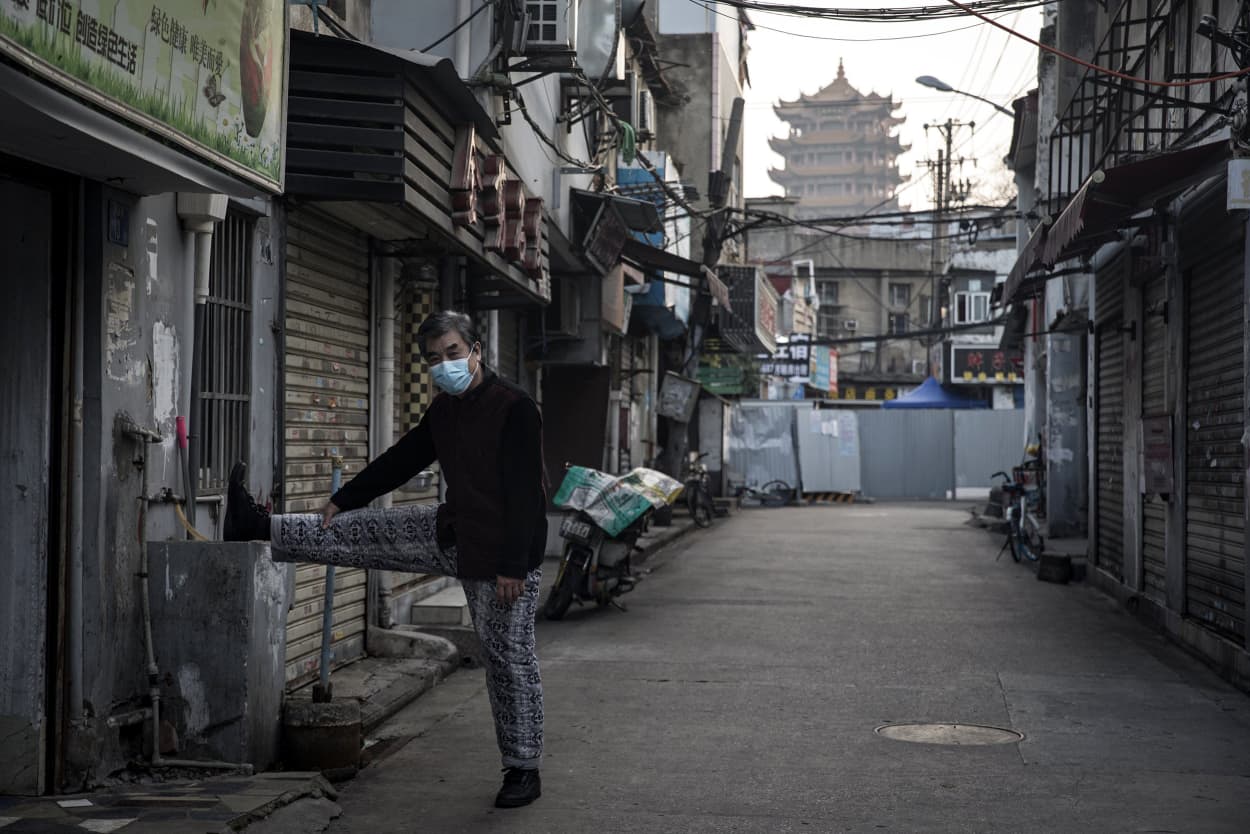 Image: A man stretches while exercising near a makeshift barricade wall in Wuhan on March 4, 2020.