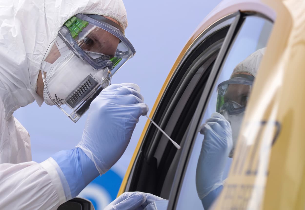 Image: A helper of the German Red Cross DRK in protective suit, left, takes a smear from a patient in his car during the official opening of a drive-through (drive-in) COVID-19 testing center at the fair ground in Dresden, eastern Germany