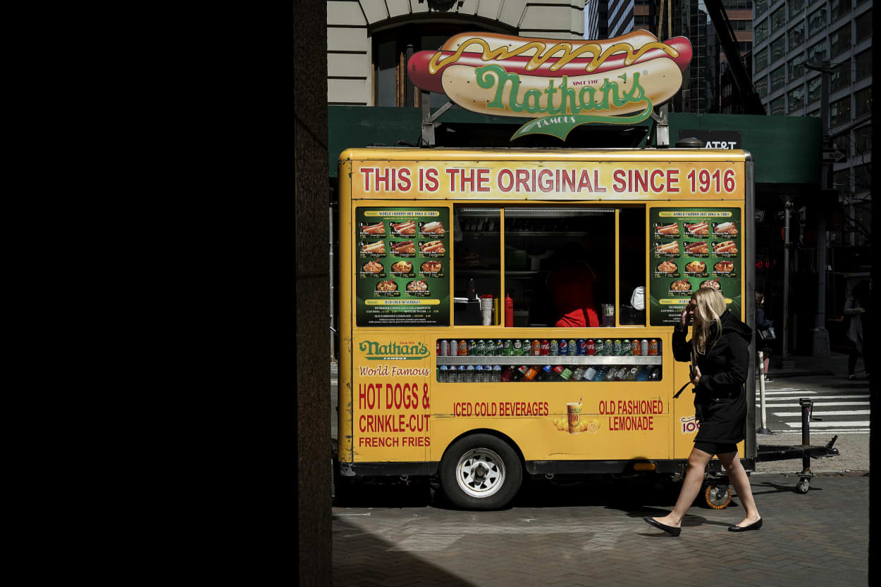 Image: A woman walks past a Nathan's hot dog cart on Wall Street in New York on April 12, 2019.