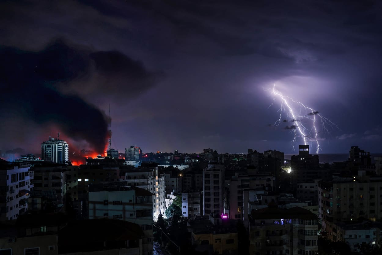 Smoke rises over Gaza from an Israeli airstrike as lightning flashes during a storm.