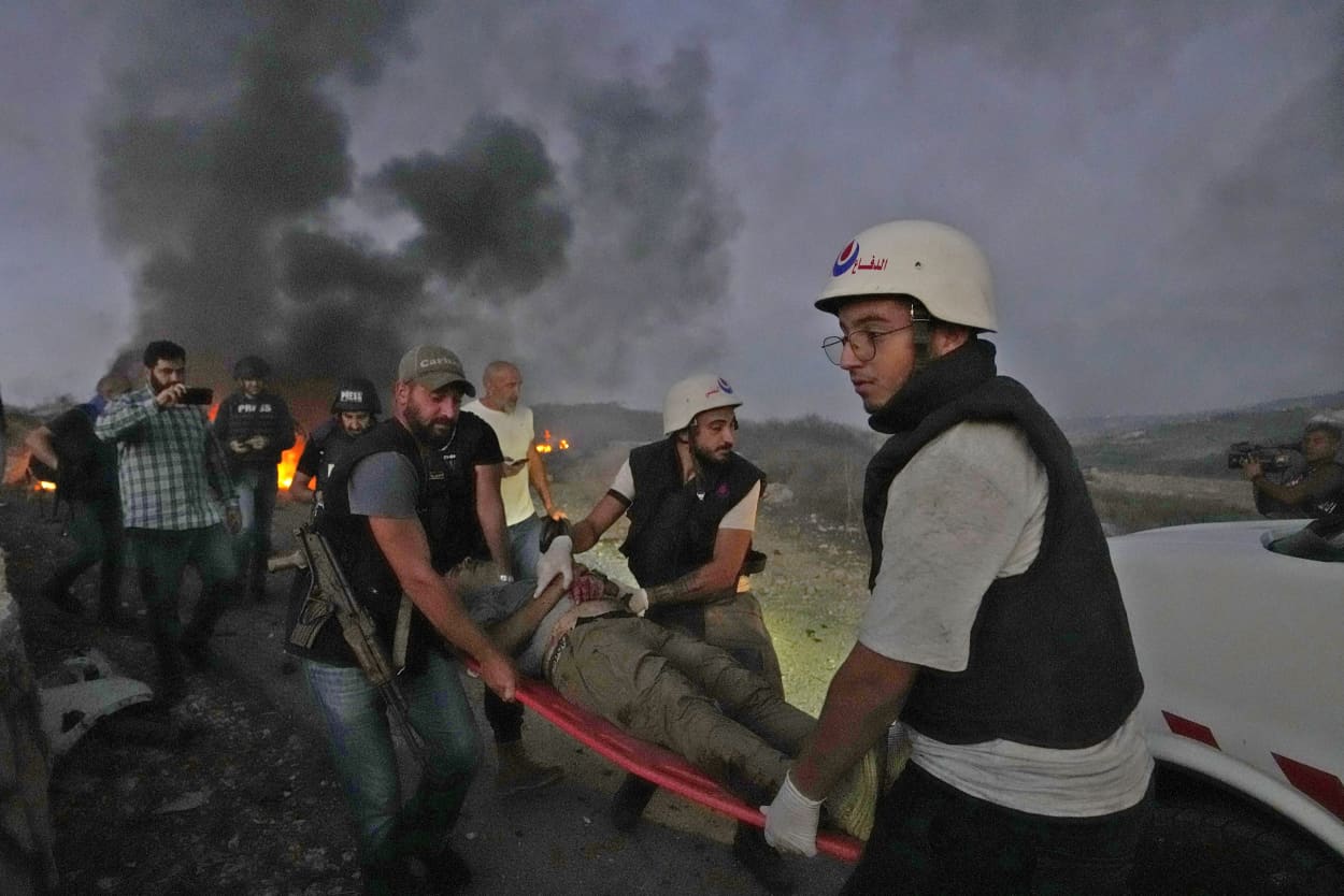 Civil Defense workers and a Lebanese security officer carry a journalist who was injured by Israeli shelling at Alma al-Shaab in south Lebanon Oct. 13, 2023.