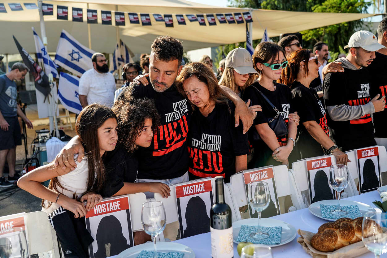 The families of Israelis who are missing or being held hostage stand by a set dinner table with empty chairs, following a deadly infiltration by Hamas gunmen from the Gaza Strip