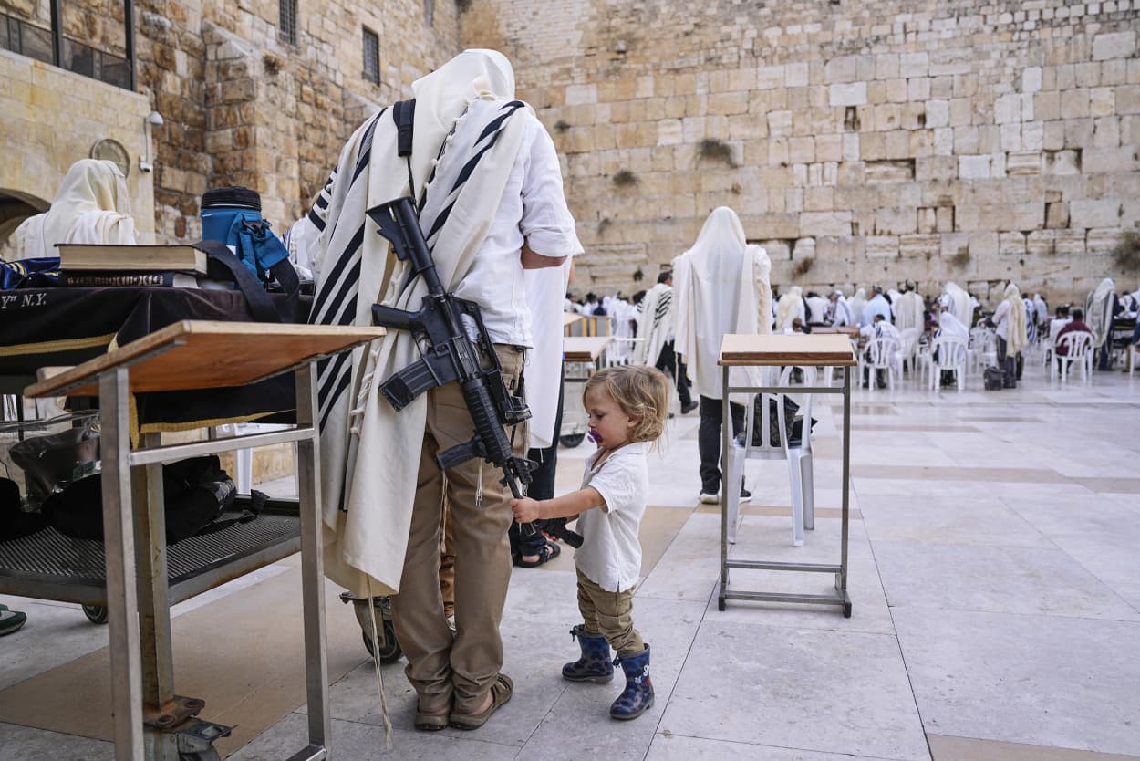 A child looks at the weapon of an off-duty member of Israel's security forces at the Western Wall, the holiest site where Jews can pray, in Jerusalem, Nov. 14, 2023. Tens of thousands of Israeli reservists have been called up for action for the war against Hamas, while other security personnel have begun to carry weapons in public.