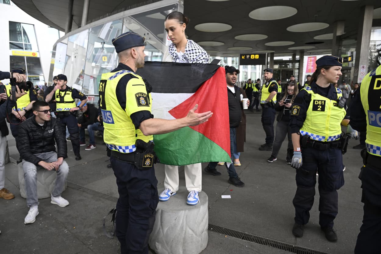 A police officer speaks to a demonstrator holding a Palestinian flag at the 68th edition of the Eurovision Song Contest (ESC) at Dagvattenparken