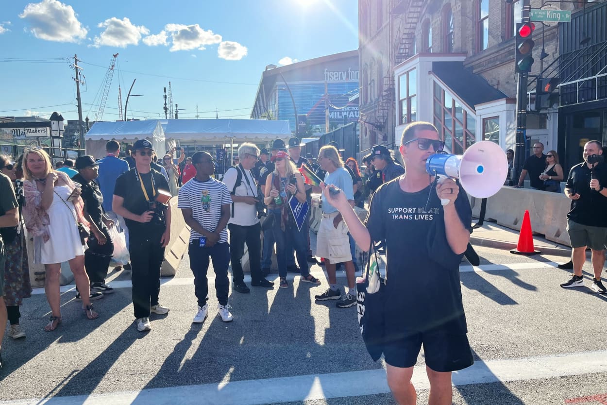 A man shouts into a megaphone at the main entrance to get into the hard security perimeter surrounding the Fiserv Forum.