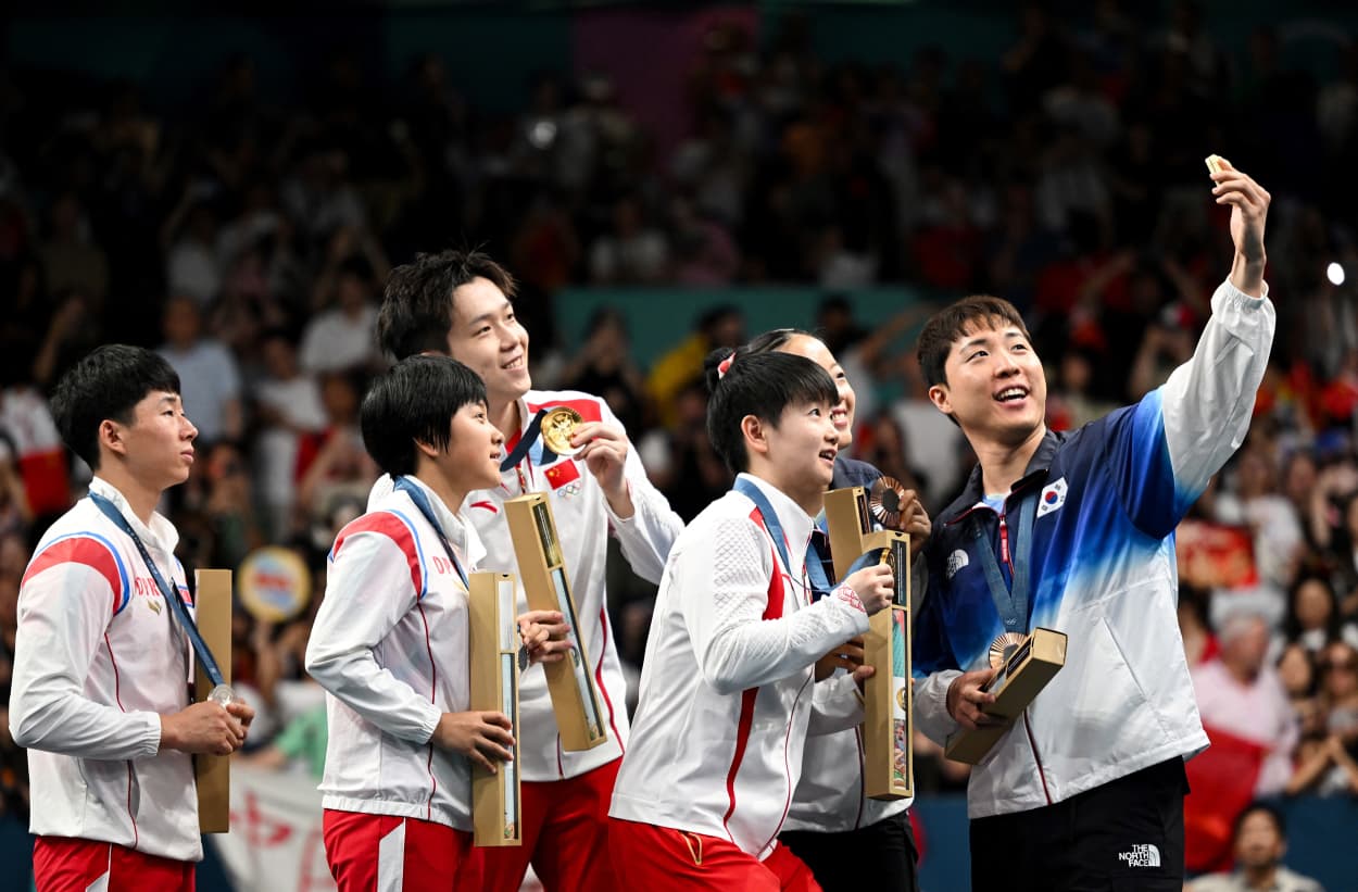 South Korea's Lim Jonghoon, right, takes a selfie with his phone as he celebrates on the podium with China's Wang Chuqin and Sun Yingsha, North Korea's Ri Jong Sik and Kim Kum Yong and South Korea's Shin Yubin at the end of their mixed table tennis doubles competition at the Olympics in Paris