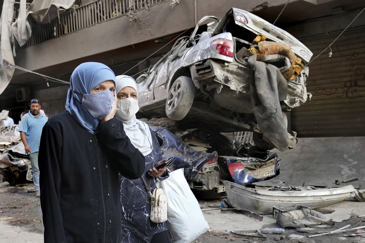 Lebanese women pass near destroyed cars at the site of an Israeli airstrike in Beirut.