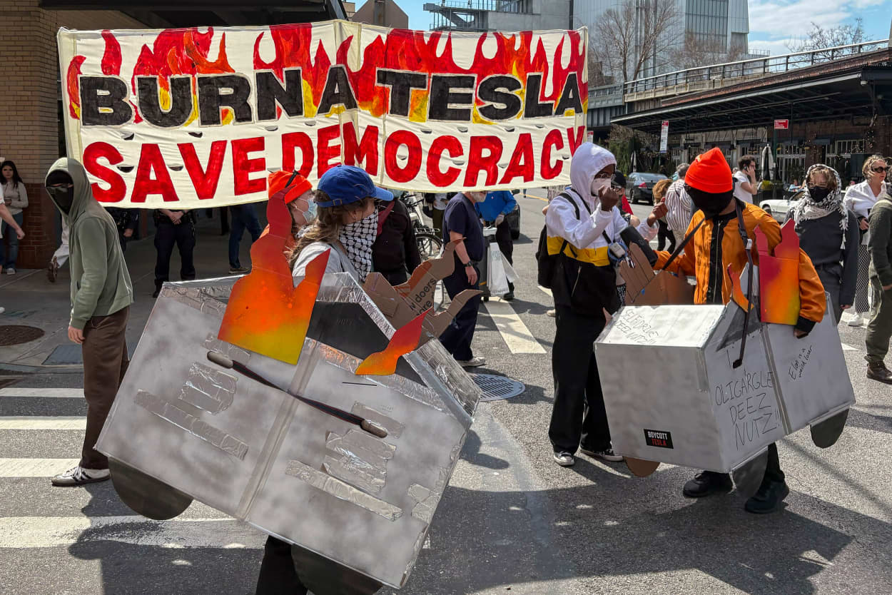 Two masked protesters were wearing what appeared to be cardboard silver cyber trucks in flames.