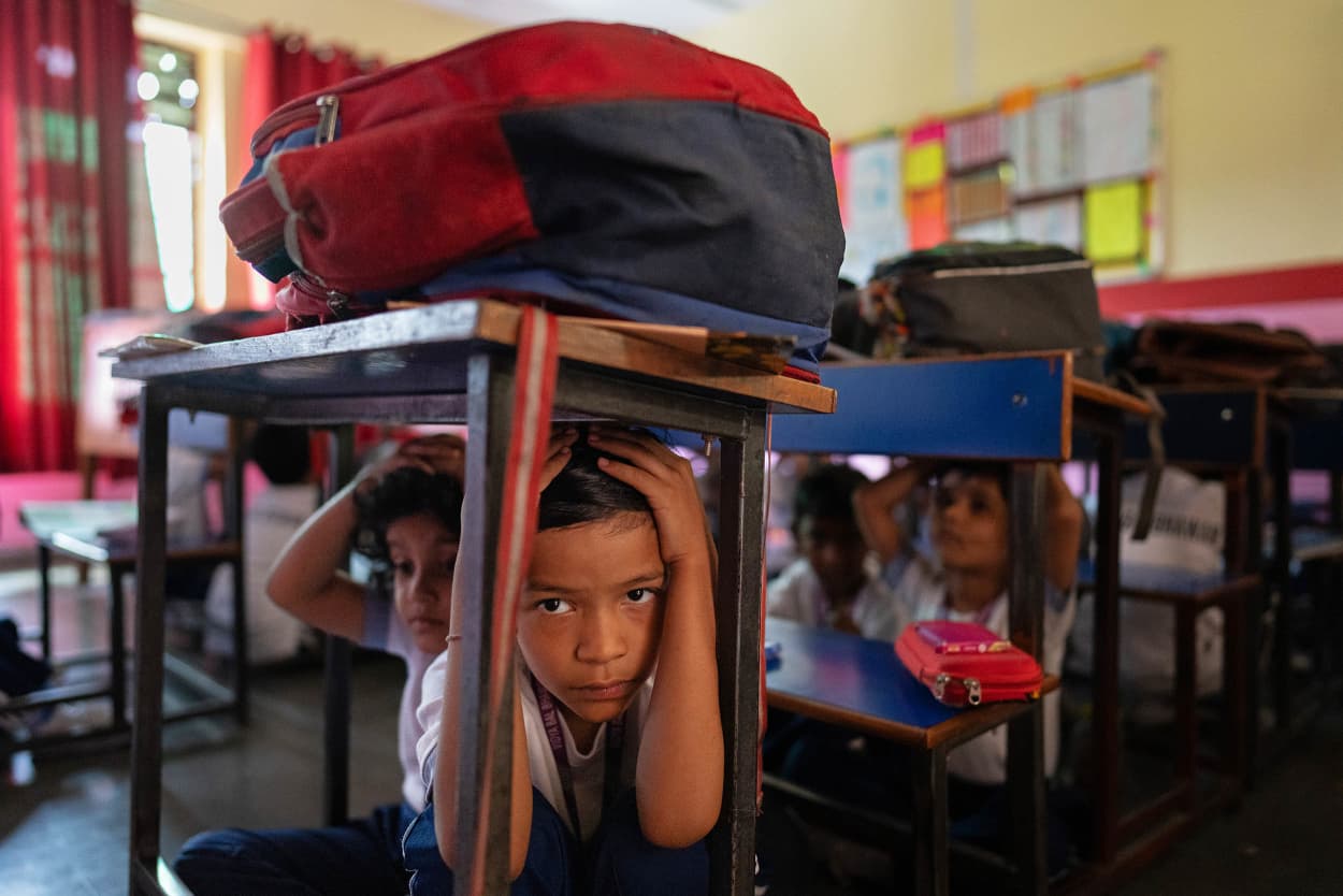 School children take shelter under their classroom desks during a mock drill