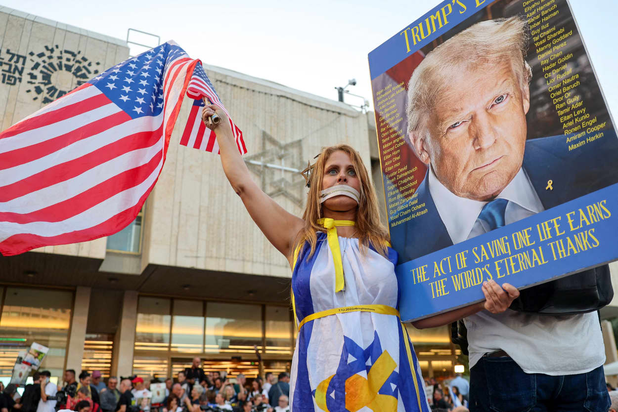 A woman draped in an Israeli flag waves that of the US and holds a picture of Donald Trump.
