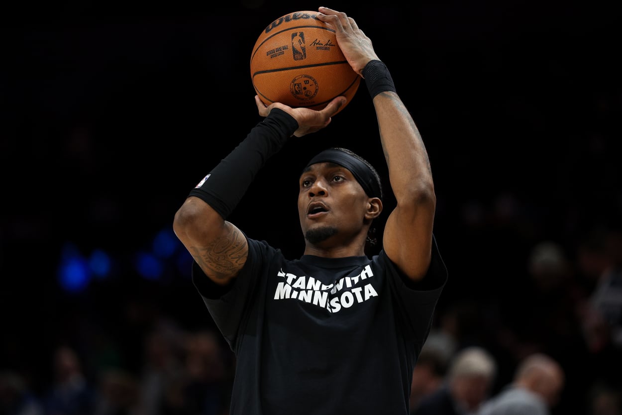 Jaden McDaniels holds a basketball over his head. He's wearing a black t-shirt with white letters reading STAND WITH MINNESOTA.