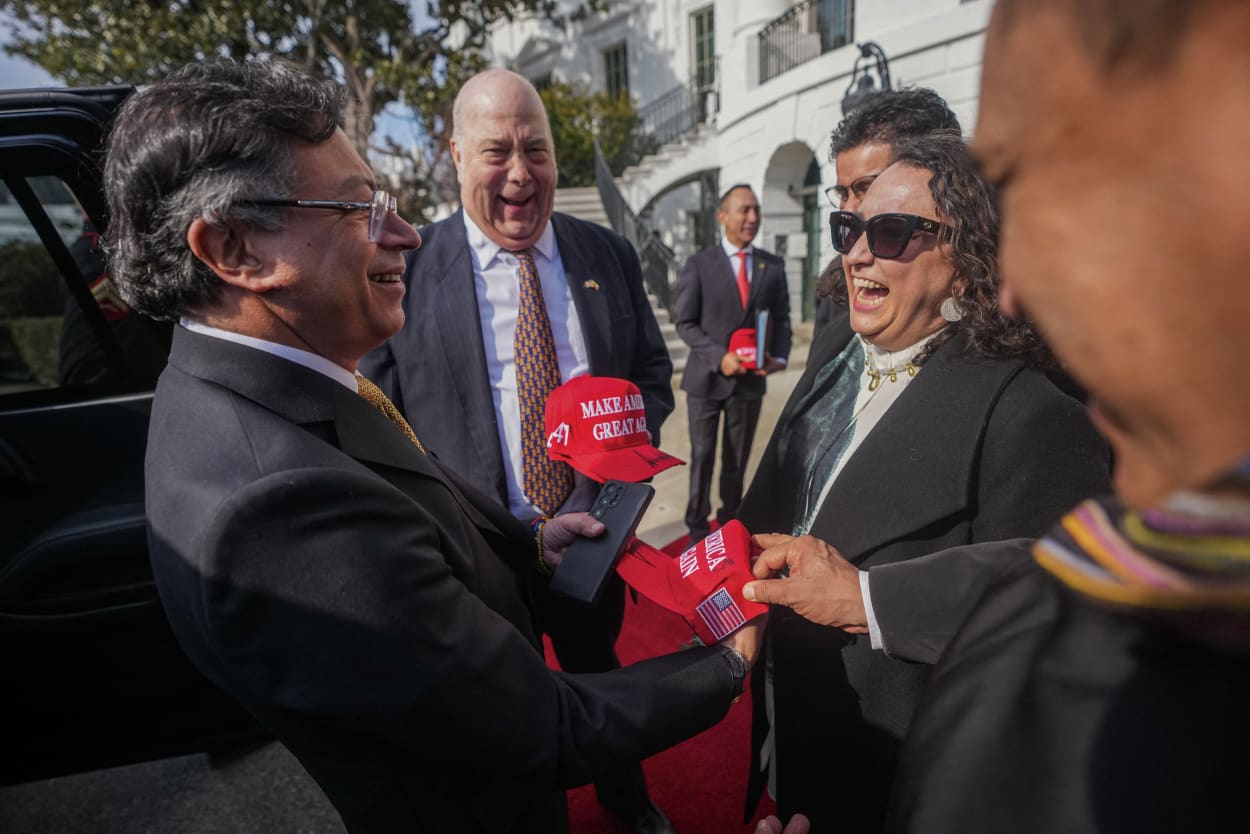 Colombian President Gustavo Petro holds a red cap in hand while standing in front of a group of people.