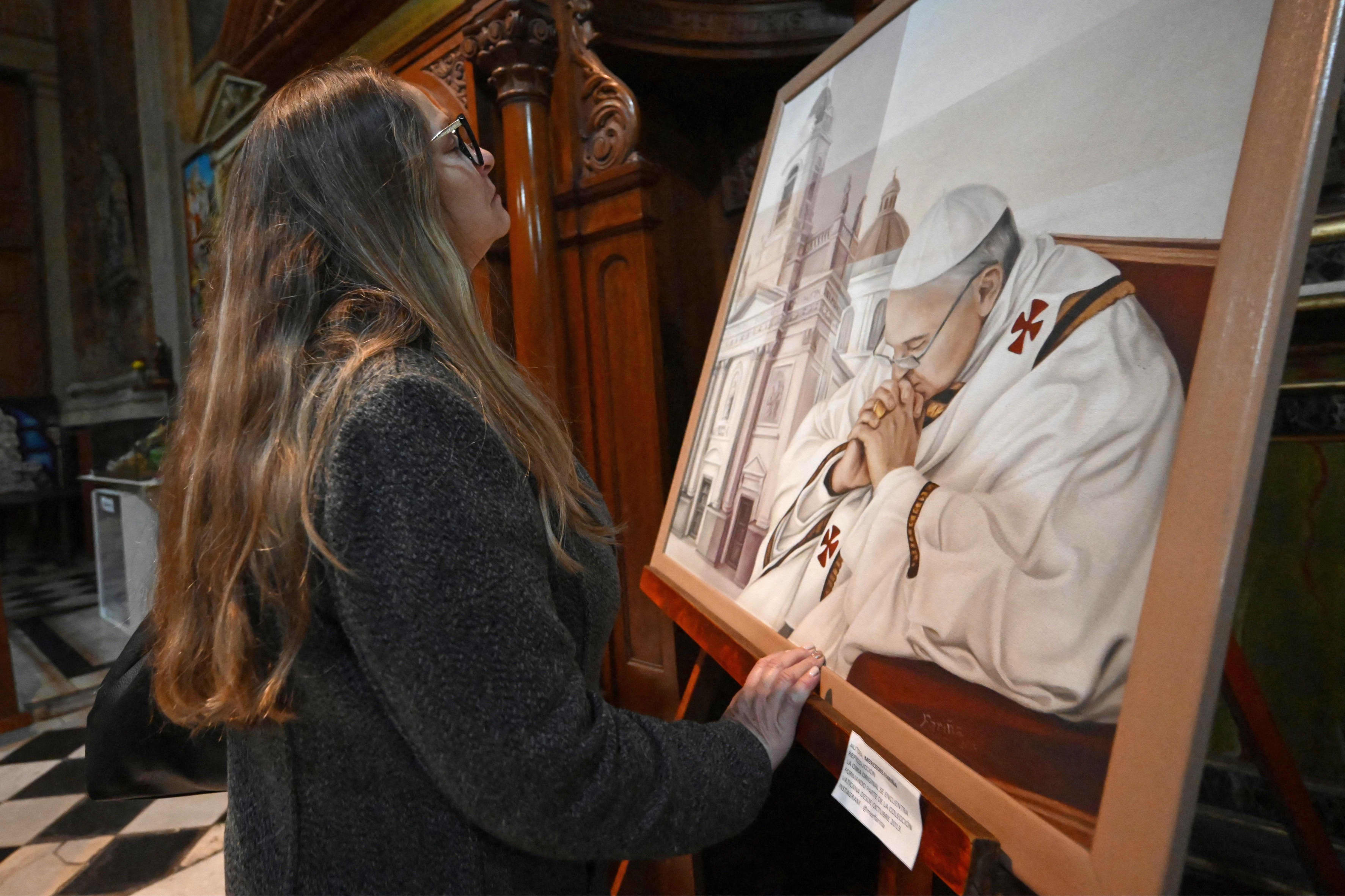 A woman prays in front of a painting of Pope Francis at Basilica San Jose de Flores in Buenos Aires on April 21, 2025. 