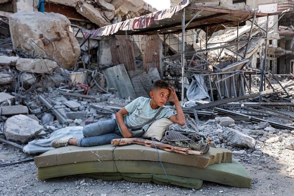 A boy lies on several foam mattresses by rubble outside a destroyed building in the center of Khan Younis 