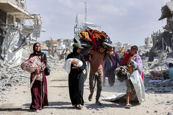 A woman carrying a child speaks with another boy as they walk with other people past the rubble of destroyed buildings in the centre of Khan Younis