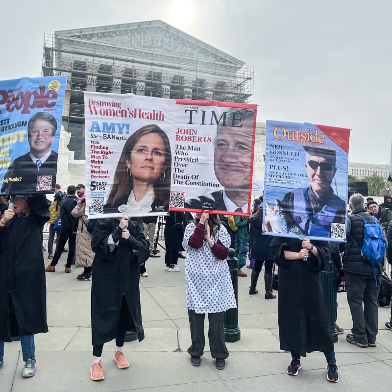 Protestors hold signs with Supreme Court justices faces
