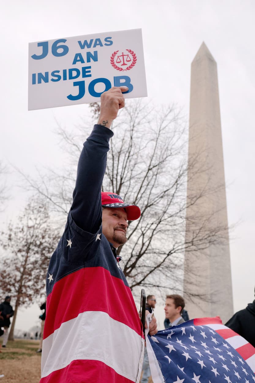  man holds a sign reading "J6 Was An Inside Job" during a January 6th memorial march marking five years since the attack.