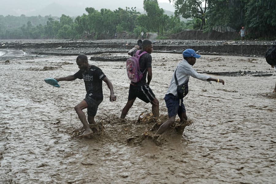 Residents wade through a flooded stream in Petit-Goave, Haiti